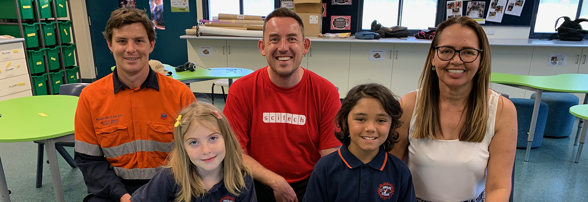 A group of three adults and two children in a classroom smiling at the camera