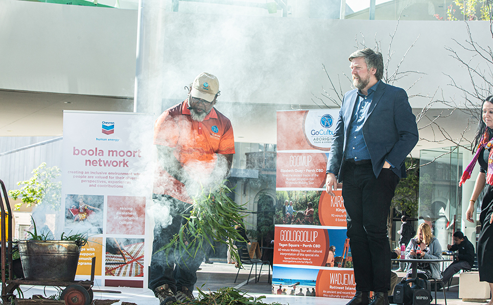 An Aboriginal man conducting a smoking ceremony with two other people standing nearby