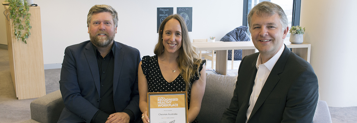 Three people sitting on a couch, the woman in the middle holding a certificate