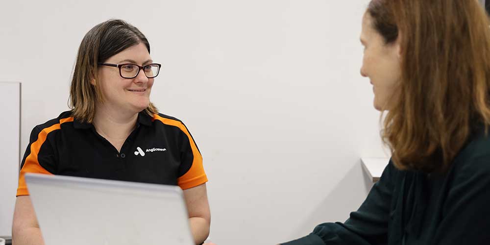 Two women talking in front of a laptop at Anglicare's offices in Perth.