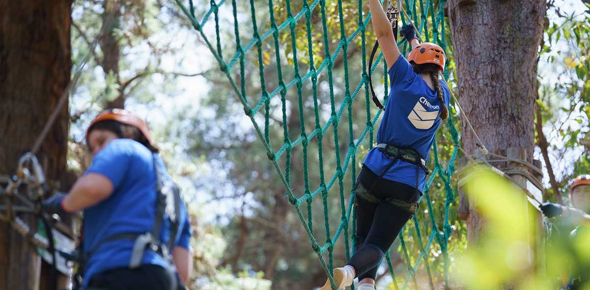 A camp hero participant completes a rope course between two trees.