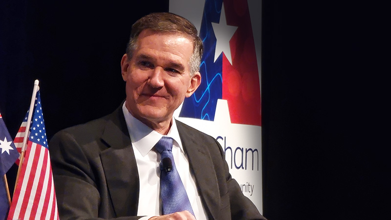 Mark Hatfield sitting in front of an AmCham Australia banner