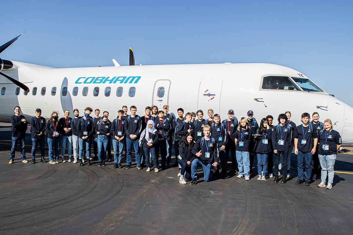 RTS On Tour students pose for group photo in front of plane 