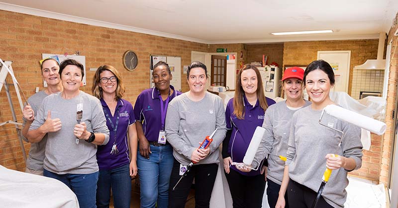 A group of women from Chevron Australia's Women's Network and Zonta House holding paintbrushes and rollers during a volunteering day at one of Zonta House's refuges.